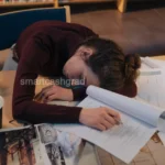 An exhausted young college student with messy hair sitting in a dark bedroom at 2 AM, face illuminated only by the glow of a laptop screen displaying graduate tuition bills.