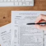 A college student at a desk reviewing a W2 tax form alongside a laptop and a calculator.