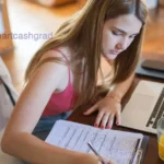 A stressed college graduate analyzing federal student loan repayment documents next to a laptop.