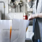 How to Apply for Food Stamps as a College Student 2026: The Exemption Blueprint A young adult placing fresh vegetables and grocery items on a kitchen counter next to a smartphone displaying a budget tracking application.