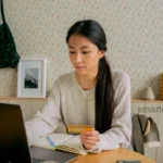 Health Insurance Options for College Students on a Budget A student holding a health insurance card in front of a laptop showing university tuition fees on screen.
